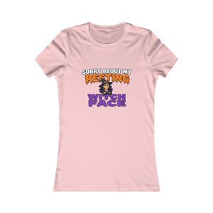 May include: A light pink short-sleeve t-shirt featuring a graphic with the text SORRY ABOUT MY RESTING WITCH FACE in orange and purple dripping letters, accompanied by a cartoon illustration of a character wearing a witch hat.