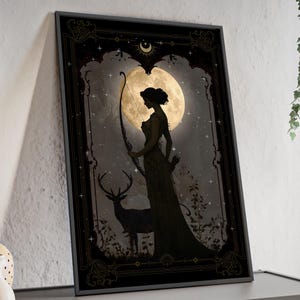 Puede incluir: Una impresi&oacute;n enmarcada en negro con un borde dorado adornado. La impresi&oacute;n presenta una silueta de una mujer con un arco y una flecha de pie frente a una luna llena. Un ciervo est&aacute; de pie a la izquierda de la mujer. El fondo es un bosque oscuro con estrellas.