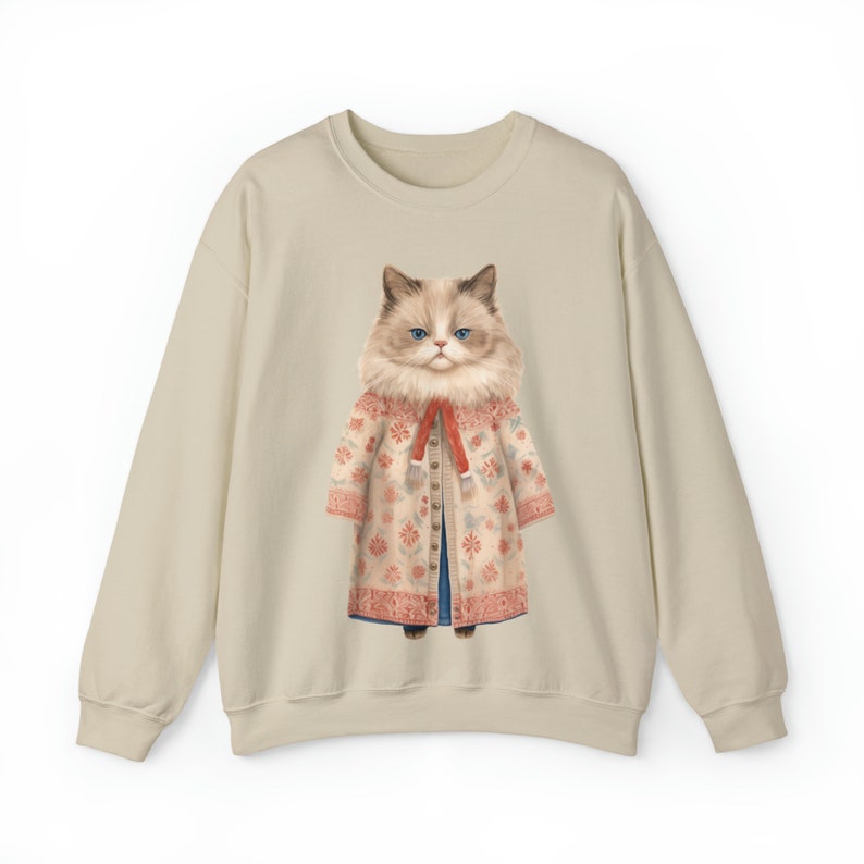 K&ouml;nnte beinhalten: Ein beiger Pullover mit einem grafischen Aufdruck eines Katers, der einen floral gemusterten Mantel und einen roten Schal tr&auml;gt.