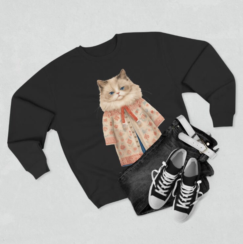 K&ouml;nnte beinhalten: Schwarzes Sweatshirt mit einer wei&szlig;en Katze, die einen floralen Pullover und ein rotes Band tr&auml;gt. Die Katze schaut in die Kamera.