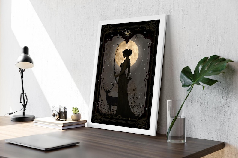 Puede incluir: Una ilustraci&oacute;n en blanco y negro de una mujer con un arco y una flecha de pie frente a una luna llena. Un ciervo se para a su lado. El fondo es un bosque oscuro con estrellas.