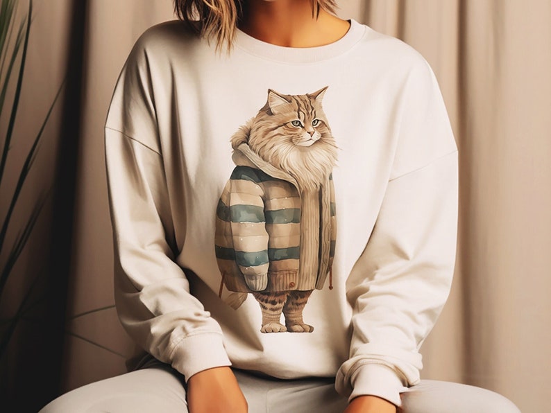 May include: A white long-sleeved sweatshirt with a graphic print of a cat wearing a striped sweater. The cat is brown and white with a fluffy tail.