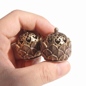 May include: Two small, round, antique brass-colored metal incense burners. Each burner features a base shaped like layered lotus petals and a removable, dome-shaped lid with intricate, openwork scroll patterns and a small knob on top.