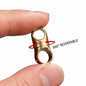 May include: A small, gold-colored metal swivel connector featuring two circular loops at opposite ends. The central section is designed to rotate, indicated by a red circular arrow graphic and the text 360° ROTATABLE printed next to it.