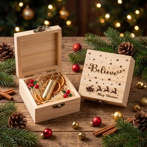 Könnte beinhalten: Zwei helle Holzkisten mit Metallverschlüssen. Eine Kiste ist geöffnet und enthält eine goldfarbene Metallkapsel mit Karabiner, eingebettet in Holzwolle und getrocknete Orangenscheiben. Die geschlossene Kiste trägt den Text Believe und Merry Christmas.