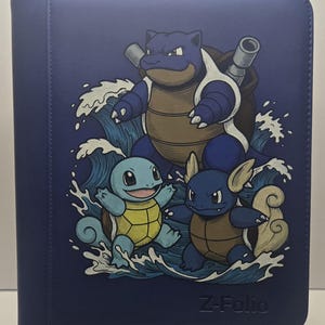 May include: A dark blue Z-Folio binder featuring a graphic illustration of three turtle-like creatures, Squirtle, Wartortle, and Blastoise, surrounded by stylized blue and white waves. The text Z-Folio is embossed in the bottom right corner.