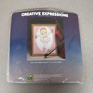 May include: A sealed crewel kit featuring a framed embroidery of a tiny ballerina in a pink tutu, surrounded by roses. The kit includes the design, fabric, and instructions. The text reads "1615 Tiny Ballerina 11" x 14" Crewel Kit".