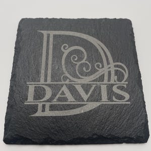 Pode incluir: Um porta-copos quadrado de ard&oacute;sia preta com uma letra D grande gravada com detalhes decorativos em volutas. O nome DAVIS est&aacute; gravado numa fonte serifada em negrito e mai&uacute;sculas no centro da letra D, criando um design personalizado.