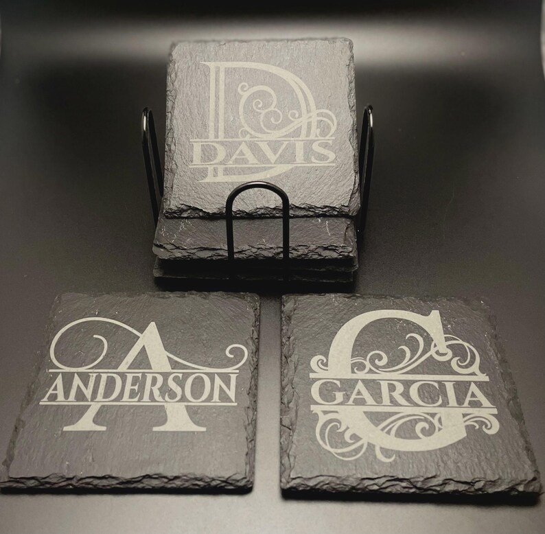 Pode incluir: Um conjunto de bases para copos quadradas em ard&oacute;sia com bordas naturais e rugosas. Cada base apresenta uma letra de monograma gravada a laser com ornamentos decorativos e um apelido, incluindo Davis, Anderson e Garcia.