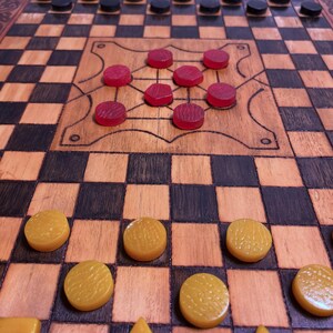 May include: A wooden board game with a checkerboard pattern. The game pieces are red, black, and yellow. The red pieces are round, the black pieces are round, and the yellow pieces are round, square, and triangular. The board has a decorative border.