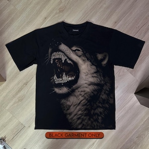 May include: A black short-sleeved t-shirt featuring a large, detailed graphic of a snarling wolf with prominent, sparkling teeth. The design is rendered in shades of grey and white against the dark fabric. The text BLACK GARMENT ONLY is visible.