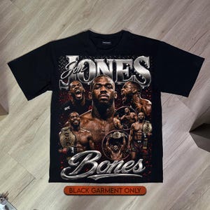 May include: A black short-sleeve t-shirt featuring a graphic print of mixed martial artist Jon Jones. The design includes multiple images of the athlete, the text "JON JONES" and "Bones" in a metallic font, and a red speckled background.