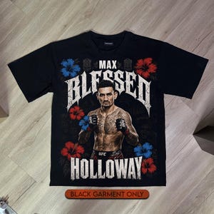 Puede incluir: Una camiseta negra de manga corta con un estampado gráfico de Max Holloway en posición de combate. El texto dice MAX BLESSED HOLLOWAY en letras blancas desgastadas. El diseño incluye flores de hibisco rojas y azules y patrones tribales.