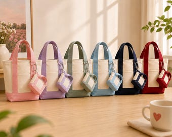 May include: A collection of six canvas tote bags in various colors: pink, purple, green, blue, navy, and red. Each bag has a matching small pouch attached. The bags are displayed on a wooden surface.