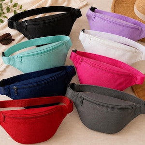 May include: A collection of colorful fanny packs in various shades, including black, purple, white, pink, teal, navy, red, and gray. Each pack features a zippered main compartment and an adjustable strap with a buckle closure. Accessories like sunglasses and a straw hat are also visible.