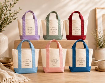 May include: Six small canvas tote bags arranged in two rows. Each bag features a cream-colored body with a colored base and handles in lavender, sage green, red, light blue, pink, or dark blue. Each bag has a front pocket with the text YOUR DESIGN HERE.