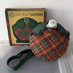 Puede incluir: Cantimplora oficial de las Girl Scouts con un estampado de cuadros rojos, verdes y amarillos. La cantimplora tiene una correa verde y est&aacute; junto a su caja original, que dice "Official Girl Scout Canteen".