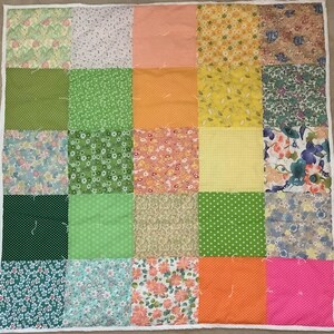 May include: A patchwork quilt with a variety of colorful fabric squares. The squares feature floral, polka dot, and striped patterns in shades of green, orange, pink, yellow, and blue. The quilt is bordered with white fabric.