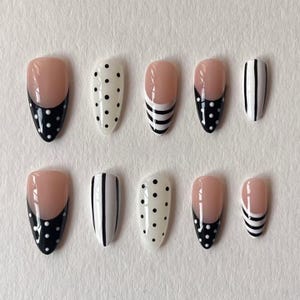 May include: A set of ten almond-shaped press-on nails featuring a variety of designs including black and white polka dots, vertical black stripes, and French-style tips with black and white polka dot accents on a nude base colour.