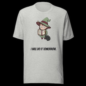 Pode incluir: T-shirt cinza claro com uma bruxa de desenho animado lendo um livro, com um gato preto aos seus pés. A bruxa usa um chapéu verde e óculos. O texto "I WILL DO IT TOMORROW" está impresso abaixo.