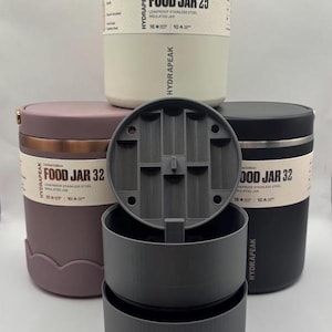 May include: Three Hydrapeak food jars in cream, mauve, and black, each with a label reading Food Jar 25 or 32, leakproof stainless steel insulated jar, 16 hours cold, 10 hours hot. A gray plastic stackable container set is positioned in the front.