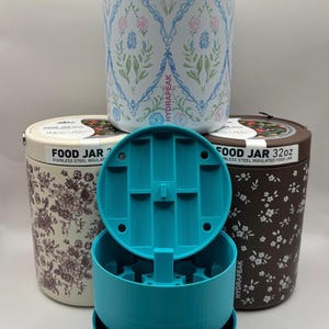 May include: Three 32oz Hydrapeak stainless steel insulated food jars with different patterns: one white with blue and pink floral trellis, one cream with dark floral sketches, and one brown with white flowers, plus a bright blue plastic insert.