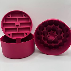 Puede incluir: Juego de tres recipientes magenta. El juego incluye una base redonda, una tapa con compartimentos rectangulares y una segunda pieza redonda con hendiduras circulares. Las piezas son de material liso.