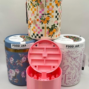 Puede incluir: Varios recipientes de alimentos aislados de acero inoxidable con diseños florales y geométricos. Uno de los recipientes tiene un interior y una tapa rosas. Los recipientes están etiquetados como "FOOD JAR 32oz" y "HYDRAPEAK".