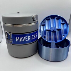 May include: A gray and blue Mavericks-themed grinder with a lid and a separate blue compartment. The grinder has the team's logo and the word "MAVERICKS" in white lettering on a blue stripe.