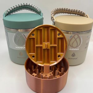 Puede incluir: Un juego de tres vasos aislados en verde y beige, con un molinillo de color cobre. Los vasos tienen asas y el logotipo "MANNA". El molinillo está abierto, revelando su mecanismo interno.