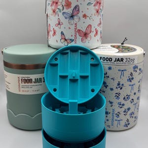 Op de afbeelding: Drie geïsoleerde Hydrapeak roestvrijstalen voedselcontainers in 25oz en 32oz maten, met bloemen- en vlinderpatronen en een saliegroene afwerking, naast een stapelbare, fel turquoise plastic container met een deksel.