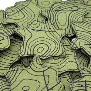 May include: A pile of green, star-shaped fabric items with black contour lines. The items have a unique, organic shape and a topographic map design. The fabric has a slightly textured appearance, and the black lines create a detailed pattern.