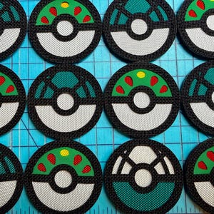 May include: A collection of twelve circular embroidered patches arranged in a grid. Each patch features a black border, a white lower half, and a green upper half with red and yellow accents, resembling a stylized spherical container.