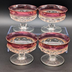 May include: A set of four clear glass dessert bowls with a wide, deep magenta band around the upper rim. Each bowl features a short, thick pedestal base and a textured, dimpled pattern on the lower exterior, finished with a thin gold trim.