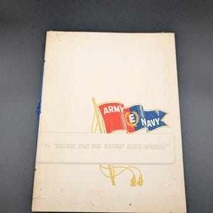 May include: A cream-colored booklet with a blue cord binding on the left side. The cover features a red, white, and blue Army-Navy E flag graphic and the text: For "ACHIEVING TODAY WHAT YESTERDAY SEEMED IMPOSSIBLE." The design includes gold accents.