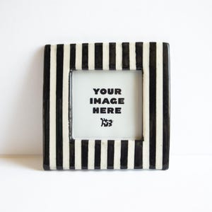 May include: A square picture frame featuring a bold black and white vertical striped pattern. The center of the frame contains a white insert with the black text YOUR IMAGE HERE and a small graphic icon located below the text.