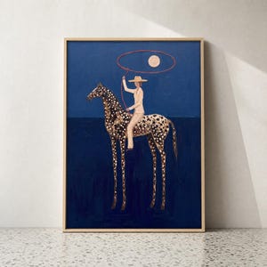 May include: A framed wall art print featuring a dark blue background with a spotted horse and a rider wearing a hat. The rider holds a red lasso loop encircling a pale moon. The horse has long legs and a dark spotted coat, standing against a deep blue horizon line.