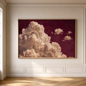 May include: A rectangular wall art print featuring a large, voluminous white cumulus cloud formation set against a deep, solid burgundy background. The artwork is enclosed in a simple, light-toned wooden frame, displaying a high-contrast sky scene.