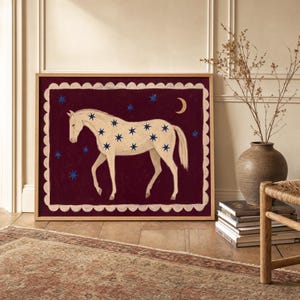 May include: A framed square wall art print featuring a cream-colored horse standing in profile against a deep burgundy background. The horse is decorated with blue stars, and a golden crescent moon and additional blue stars surround it.