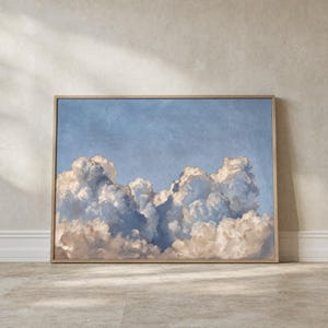 May include: A rectangular wall art print featuring a detailed painting of voluminous white and cream-coloured cumulus clouds set against a soft, textured blue sky. The artwork is encased in a thin, light-toned wooden frame.