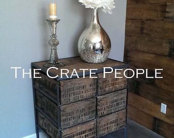 May include: A wooden crate end table with black metal legs. The table has six drawers with labels that read "Zoria Farms Inc. Brentwood & Madera San Jose CA. 1992". A silver vase with a white flower sits on top of the table.