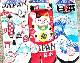May include: Three pairs of socks with Japanese-themed graphics. The white pair features a geisha, crane, and Mount Fuji. The red pair shows a beckoning cat and the text Japan. The blue pair depicts a large wave and the text 日本.