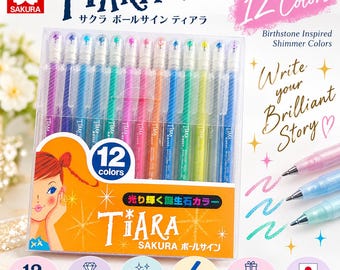 May include: A set of 12 Sakura Tiara gel ink ballpoint pens in a clear plastic case. The pens feature birthstone-inspired shimmer colors. The packaging includes the text Tiara Gel Ink Ballpoint Pen, 12 Colors, and Write your Brilliant Story.