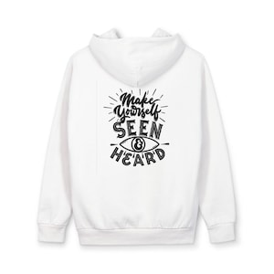 Peut inclure: Sweat à capuche blanc avec cordon de serrage et manches longues. Le dos présente un graphisme noir avec le texte "Make Yourself SEEN & HEARD" et un symbole d'œil. Vêtement décontracté et confortable.