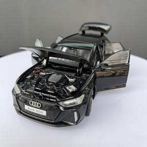 Könnte beinhalten: Ein schwarzes Audi RS6 Modellauto mit geöffneter Motorhaube, die Motordetails zeigt, sowie geöffneten Seitentüren und einem geöffneten Kofferraum. Der Frontgrill trägt das Audi-Logo und ein Nummernschild mit der Aufschrift Audi RS6.