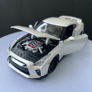 May include: A white model car with the bonnet and door open, revealing the engine. The car has black wheels and a spoiler. The engine is detailed with red and silver components.