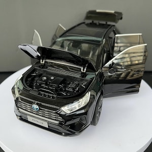 Op de afbeelding: Een zwart Toyota RAV4 schaalmodel met een geopende motorkap, open zijdeuren en een open achterklep. De grille aan de voorzijde is voorzien van een blauw Toyota-embleem en een nummerplaat met de tekst RAV4. De motorruimte is onder de kap zichtbaar.