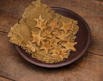 May include: A dark brown, shallow, round dish holds a square of burlap and several star-shaped cookies. The cookies are light brown and arranged on the burlap. The dish sits on a wooden surface.