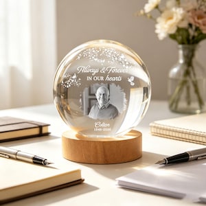 May include: A clear glass sphere with a photo of a man, resting on a wooden base. The sphere has the text "Always & Forever in our hearts" and the name "Colton" with the years 1946-2026. A memorial keepsake.