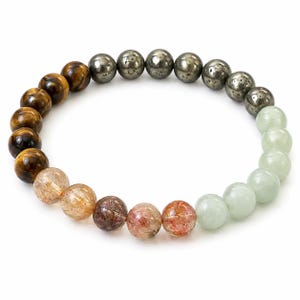 May include: A stretch bracelet composed of round beads in varying colors and textures. The design features brown tiger eye, metallic grey pyrite, translucent pale green jade, and clear quartz beads with reddish-brown needle-like inclusions.